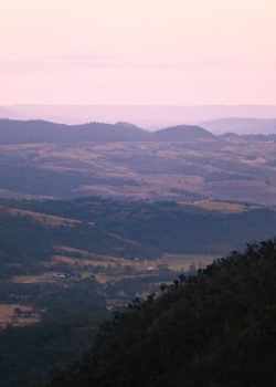 Rolling hills and mountains under a pink sky.